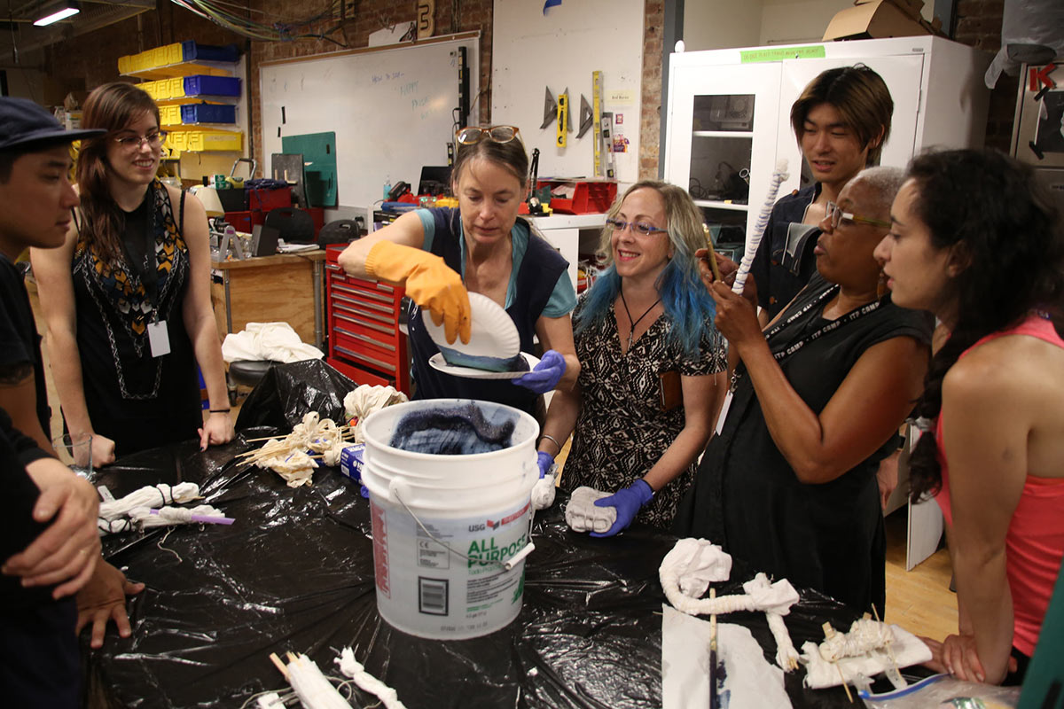 A group of students in the shop watching a demonstration using slime material